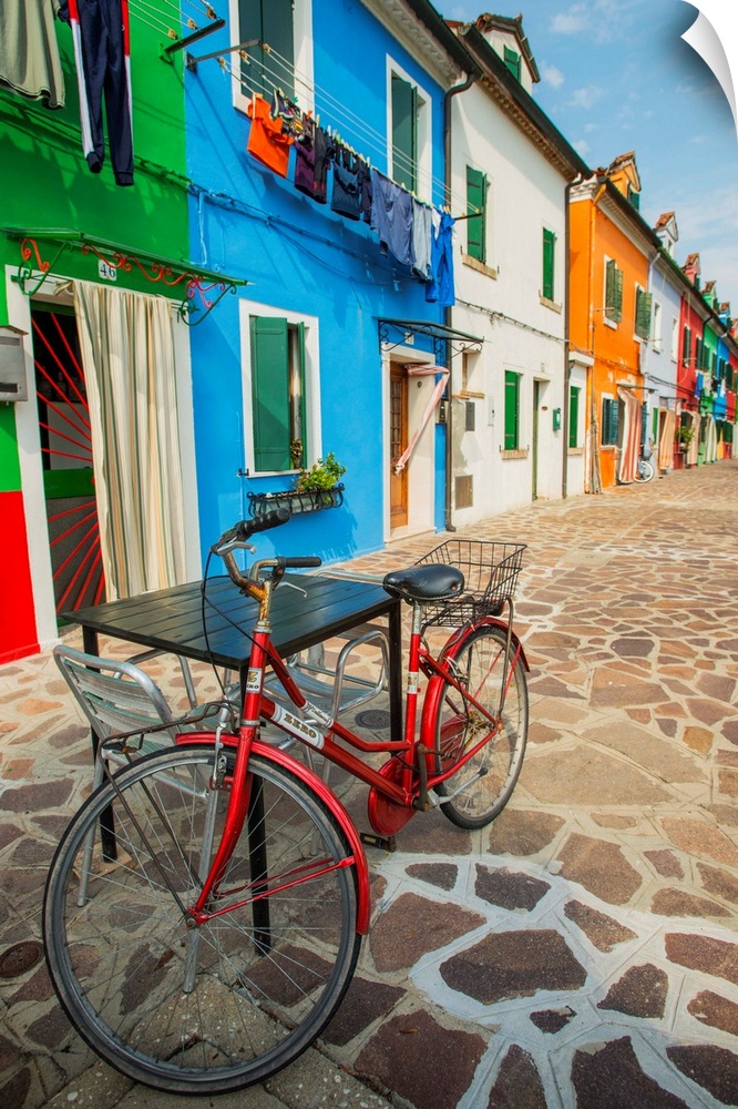 Photograph of a red bicycle leaning on a table outside of a row of vibrant fishermen's homes in Burano.