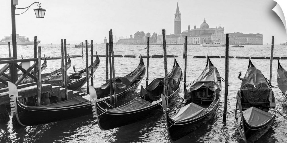 Black and white photograph of a row of gondolas in front of Piazza San Marco (St. Mark's Square) in Venice, Italy.