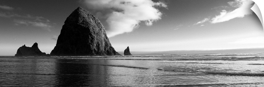 Black and white panoramic photograph of Haystack Rock with rippling waters.