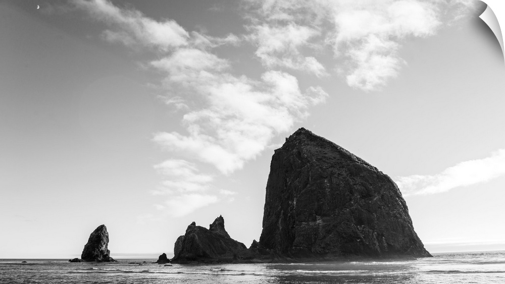 Black and white photograph of Haystack Rock with the moon in the top corner.