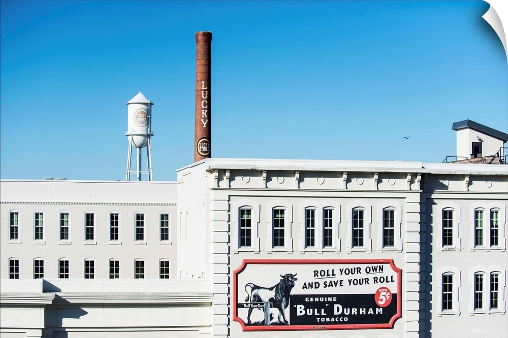 Bull Durham tobacco advertisement on a building facade, Lucky Strike water tower and smokestack in the distance, Durham, N...