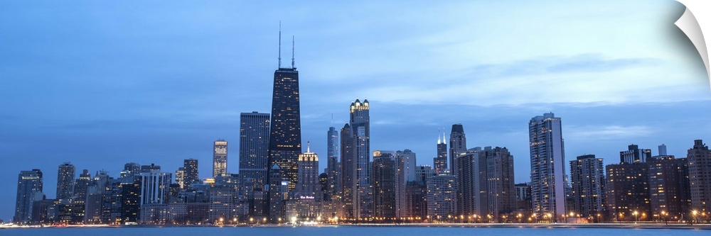 Panoramic view of the Chicago city skyline illuminated in the early evening, seen from across the water.