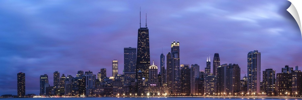 Panoramic view of the Chicago city skyline illuminated in the early evening, seen from across the water.