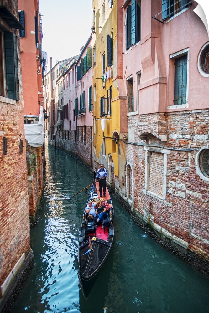 Photograph of a gondola rowing though a canal surrounded by colorful building facades in Venice, Italy.