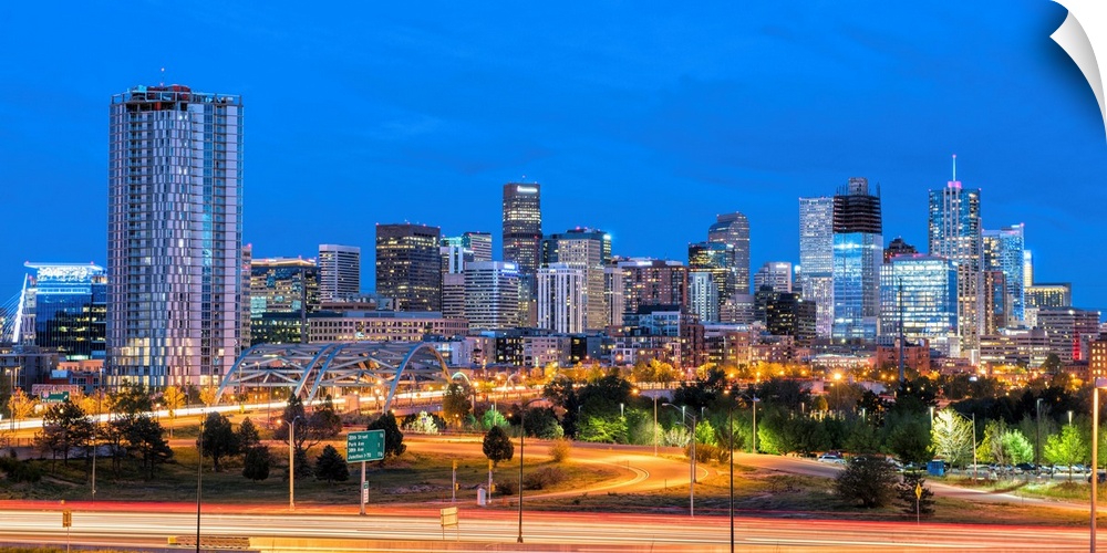 Photograph of the Denver, CO skyline at dusk with warm light trails on the highway from passing cars.
