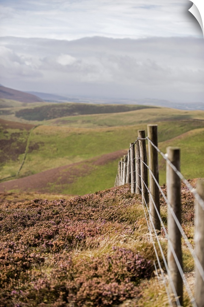 Vertical photograph of a fence running though rolling hills in an Edinburgh countryside, Scotland, UK
