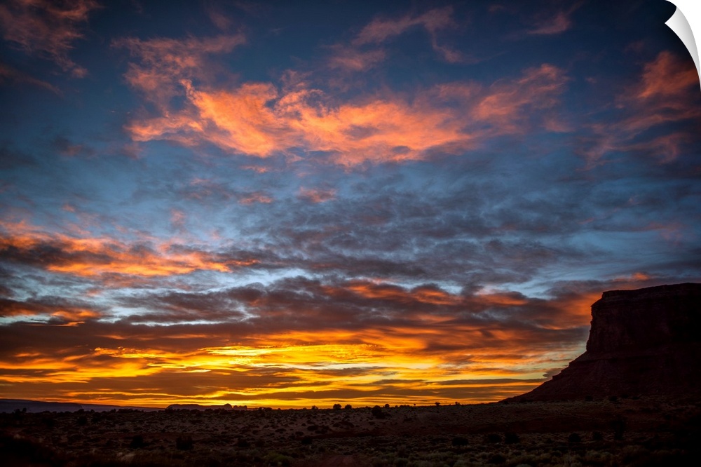 Vibrant yellows and red dapple the sky as the sun sets over Eagle Mesa in Monument Valley, Utah.