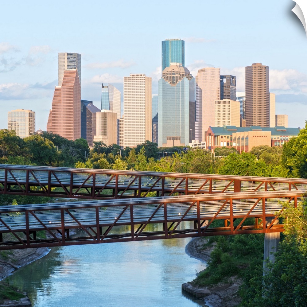Square photograph of the Houston TX skyline in the distance with the  Rosemont pedestrian bridge in the foreground over th...