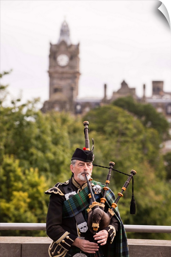 Photograph of a man playing the bagpipes in Edinburgh with the clock tower blurred out in the background.