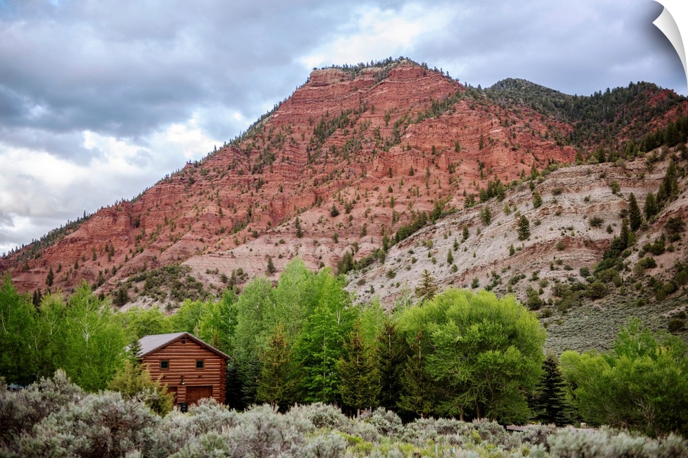 Photo of a wood cabin nestled with trees under a mountain cliffside in Colorado.