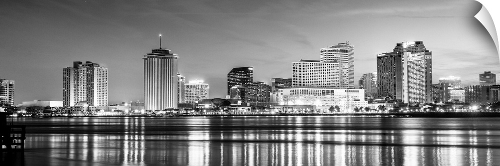 Panoramic photograph of the New Orleans skyline lit up at night with reflecting bands onto the Mississippi River.