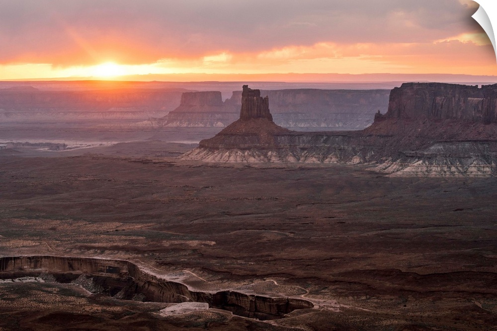 The sun setting on the horizon behind sandstone rock formations, over White Rim Trail, Canyonlands National Park, Moab, Utah.