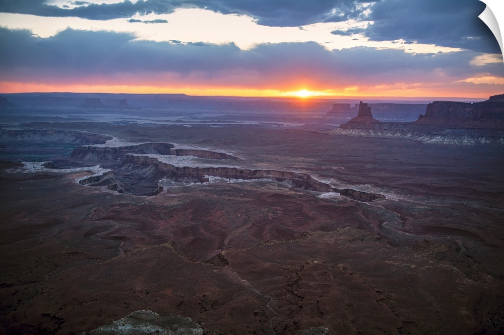 The sun setting on the horizon behind sandstone rock formations, over White Rim Trail, Canyonlands National Park, Moab, Utah.