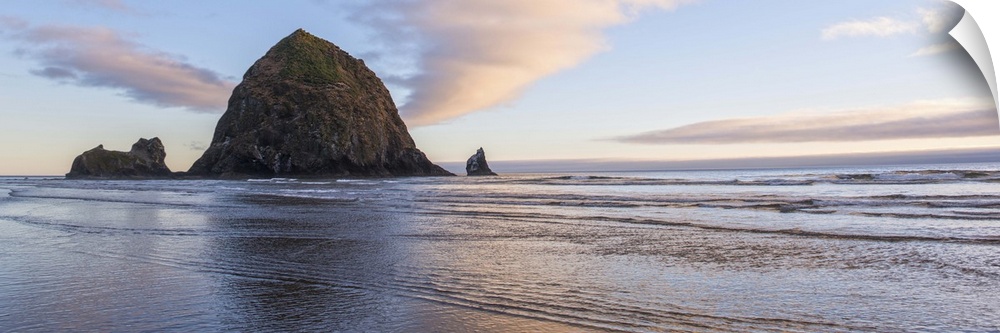 Panoramic photograph of Haystack Rock with a pink and purple sunset and reflections on the water.