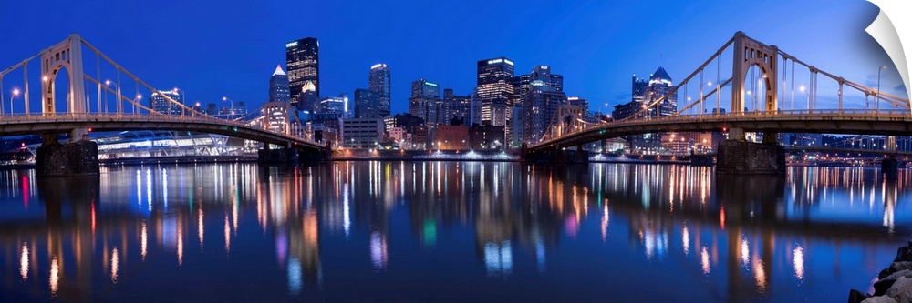 Panoramic view of the Pittsburgh city skyline in the evening reflected in the water, with two of the Three Sisters bridges...