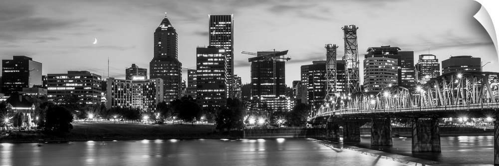 Panoramic photograph of the Portland, Oregon skyline lit up with lights at the beginning of sunset with a small crescent m...