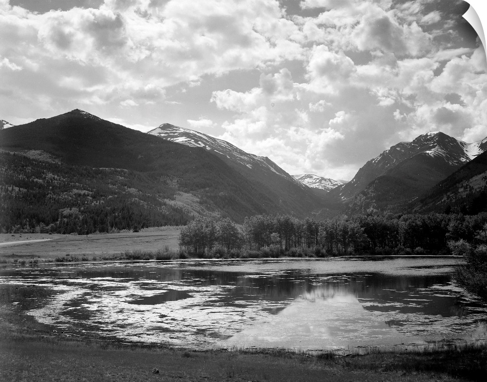 In Rocky Mountain National Park, lake and trees in foreground, mountains and clouds in background.