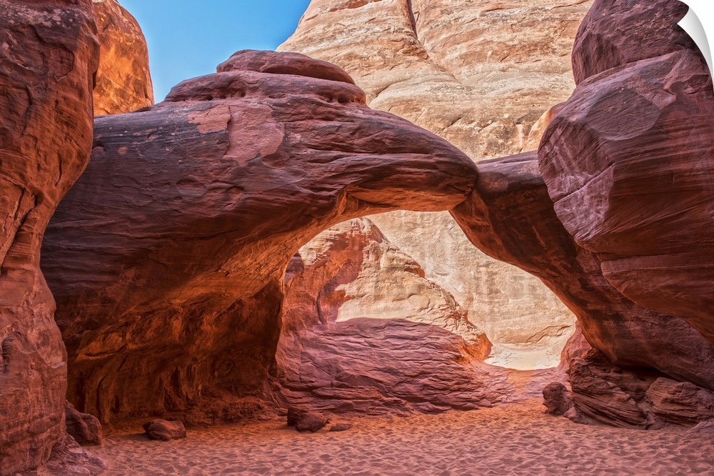 Sunlight illuminates the red sandstone of the Sand Dune Arch and the sandy trail below, Arches National Park, Moab, Utah.