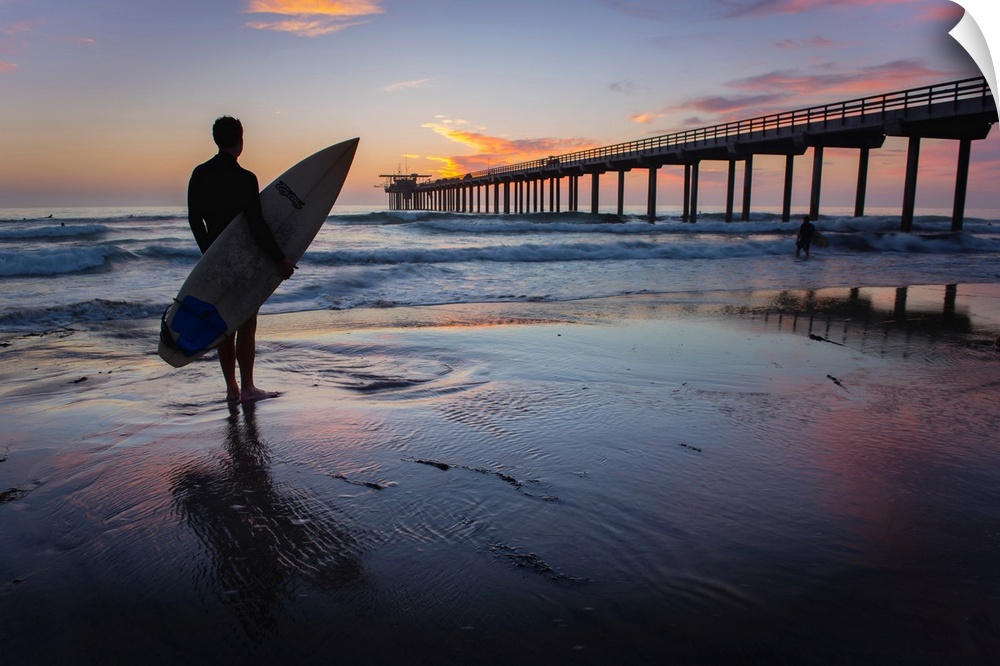 Silhouetted photograph of a man holding a surf board on the shore of Ocean Beach in San Diego, California, with the Ocean ...