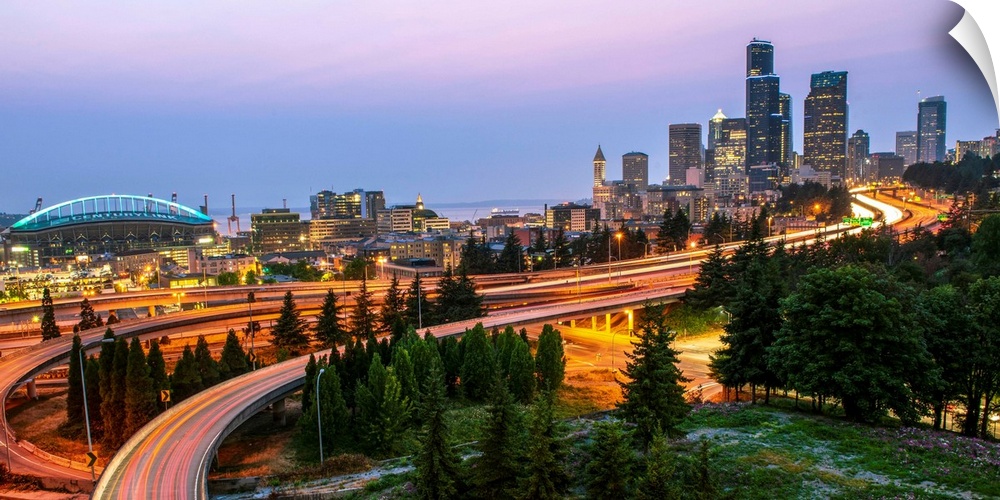 Panoramic photograph of the Seattle skyline at night with light trails from the car lights on the highway.