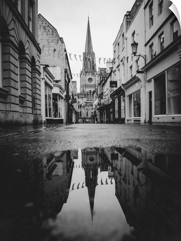 Black and white photograph of St. Michael's Church reflecting into a puddle in the middle of a street in Bath, England.
