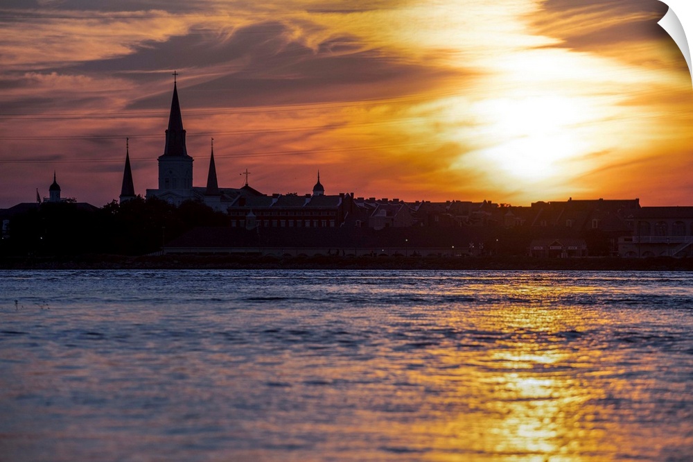 The sun sets on the Mississippi River with view of the silhouette of St. Louis Cathedral in New Orleans, Louisiana.