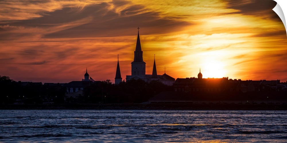 The sun sets on the Mississippi River with view of the silhouette of St. Louis Cathedral in New Orleans, Louisiana.