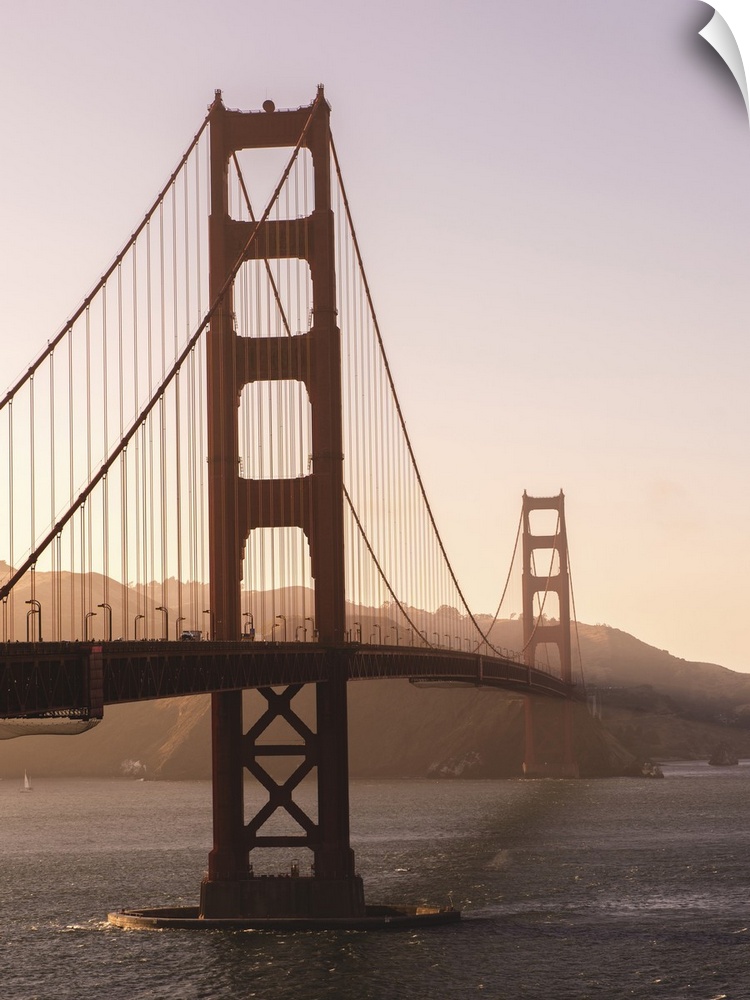 Photograph of the Golden Gate Bridge with warm hues from the sunset and light fog.