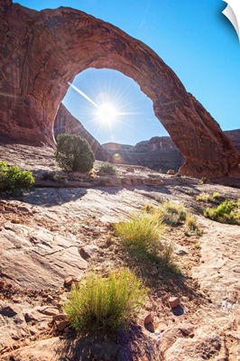 The sun shining behind the Corona Arch in Arches National Park, Utah