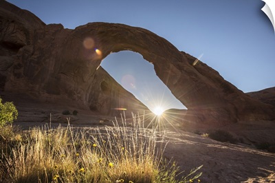 The sun shining behind the Corona Arch in Arches National Park, Utah