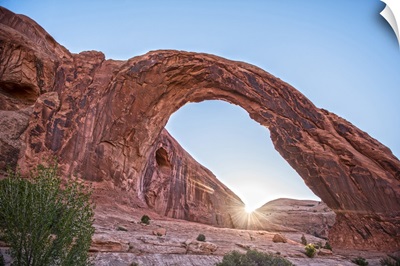 The sun shining on the horizon behind the Corona Arch, Arches National Park, Utah.