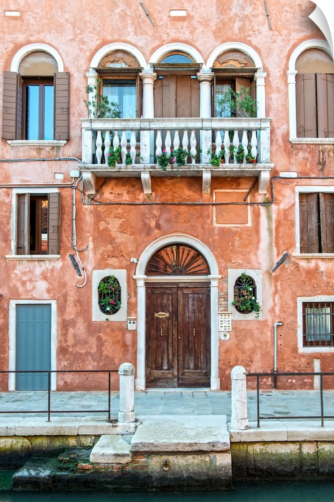 Photograph of a salmon colored facade in Venice with a door, windows, and a balcony.