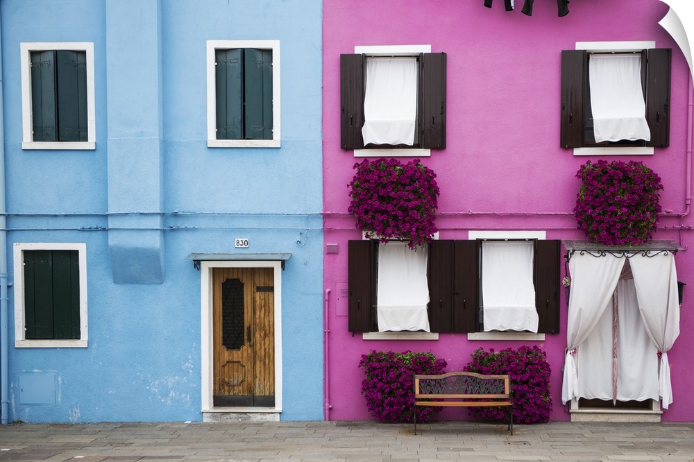 Photograph of a colorful Venice Facade with a wooden door, windows, and magenta potted flowers on the walls.