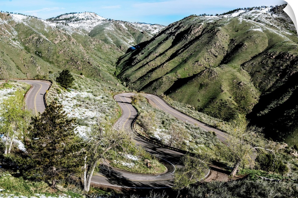 Photo of a winding road below a mountain slightly covered in snow in Colorado.