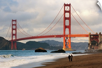 A couple strolling on Baker Beach near the Golden Gate Bridge at dawn