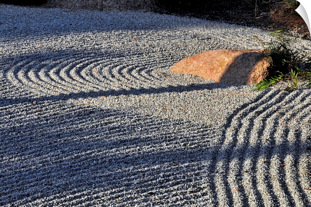 An embedded rock catches the afternoon sun in a raked rock garden.