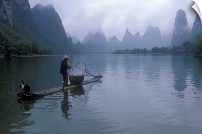 Cormorant fisherman poles a bamboo raft near limestone karst mountains, Li River, People's Republic of China