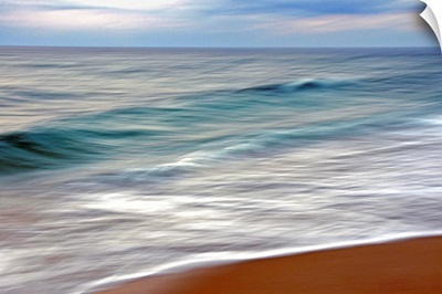 Teal and white surf flows on a rust-colored beach under blue clouds