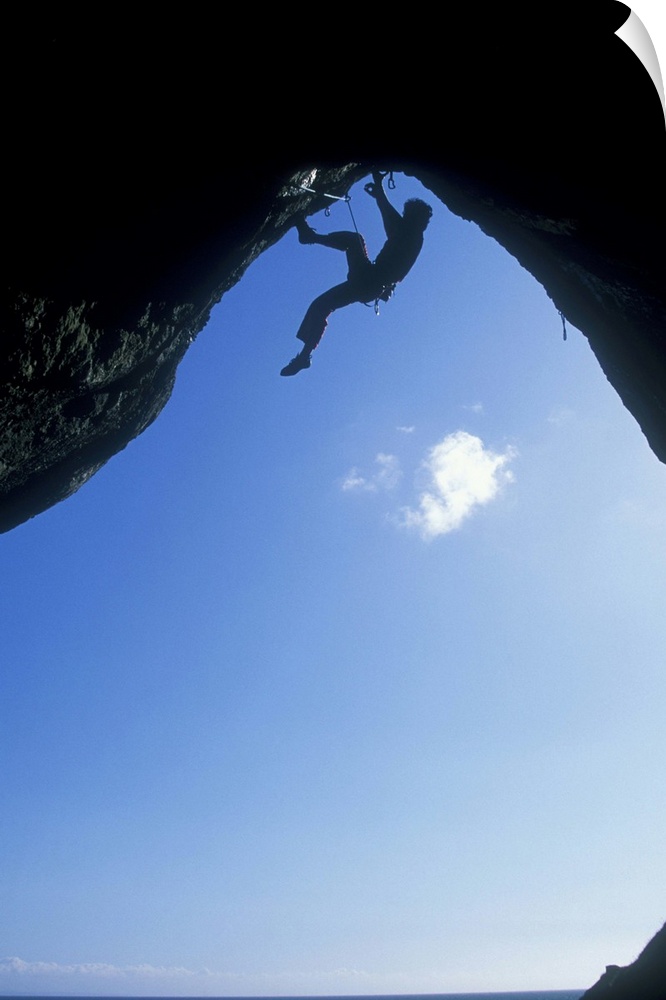 A climber ascending a cave archway at Foxhole, Gower Peninsula, Wales, UK