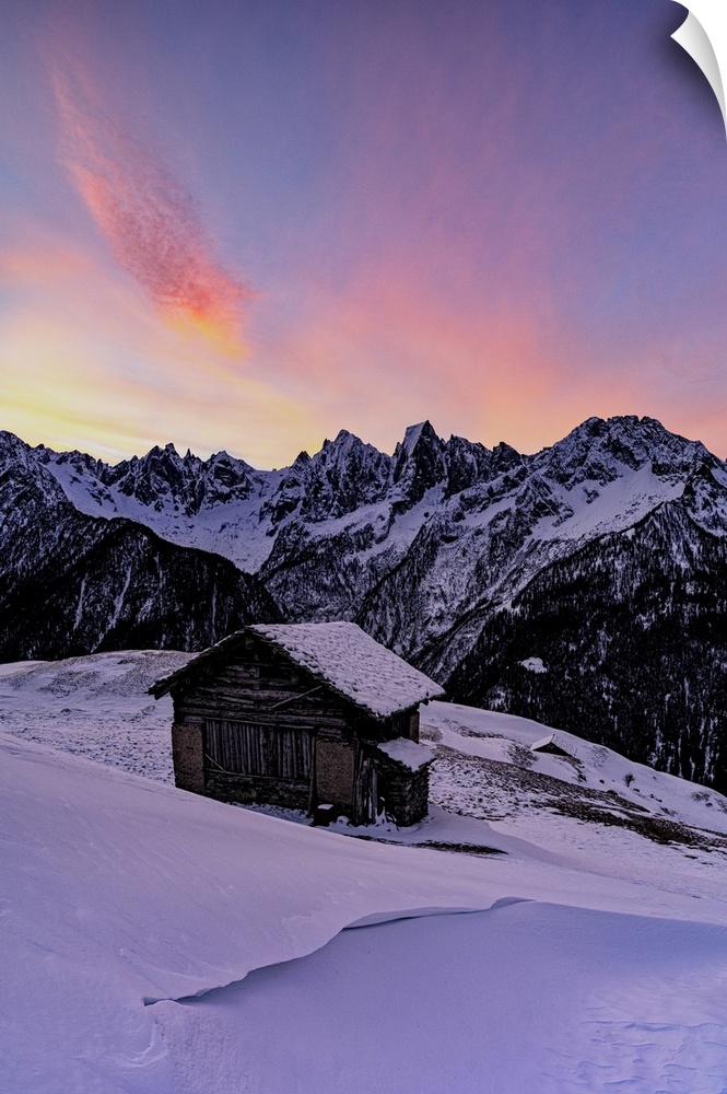 Lone mountain hut in deep snow with majestic peaks in the background at dawn, Tombal, Val Bregaglia, Graubunden, Switzerla...