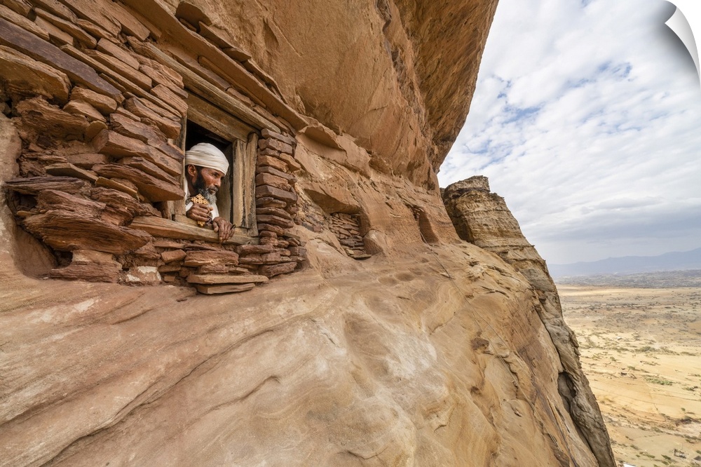 Priest looking out from a small window carved into rocks in Abuna Yemata Guh church, Gheralta Mountains, Tigray Region, Et...