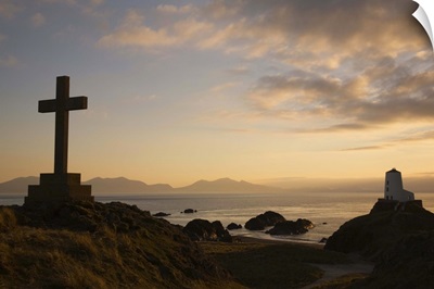 Stone Cross and old lighthouse in silhouette at sunset, Anglesey, North Wales, UK