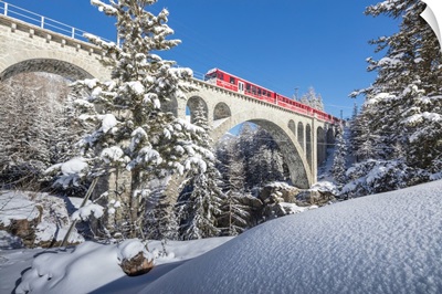 The red train on viaduct surrounded by snowy woods, Cinuos-Chel, Engadine, Switzerland