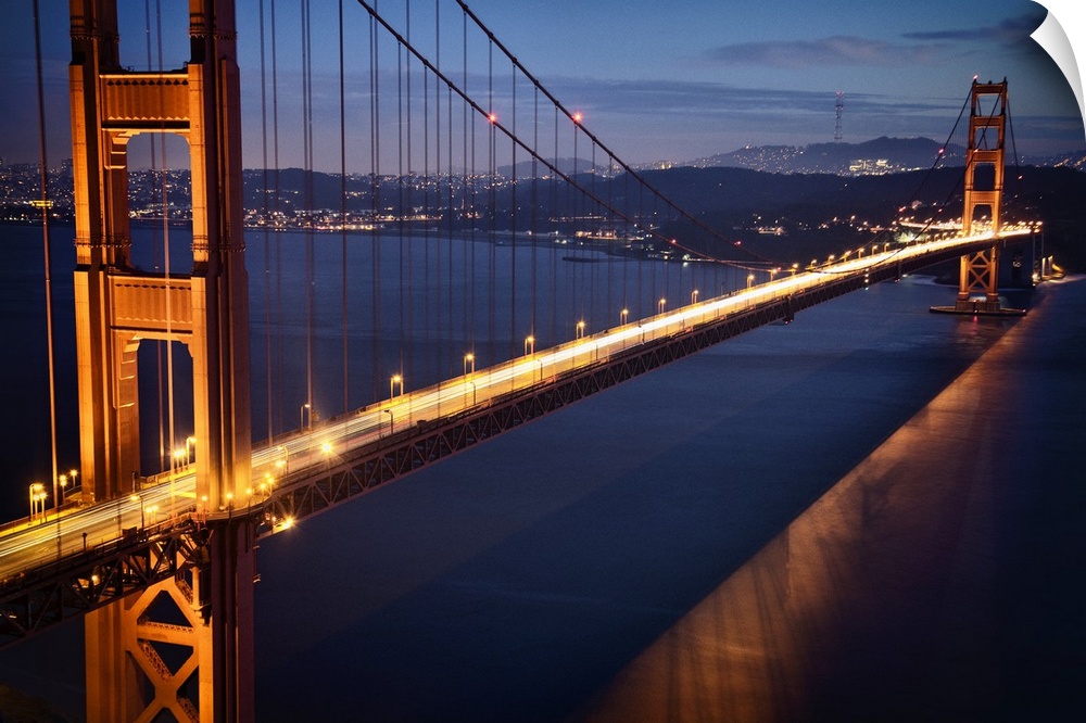 Aerial photograph of the famous Golden Gate Bridge in the evening, glowing with light trails from traffic, in San Francisco.