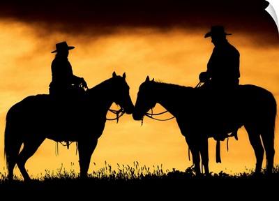 Cowboy and cowgirl on horseback in silhouette at sunset