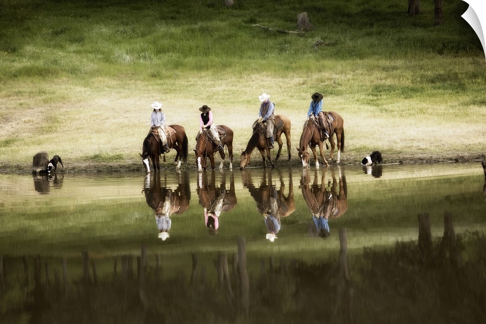 Photograph of horseback riders and their dogs by water at dusk.  The riders and horses and reflected in the water.
