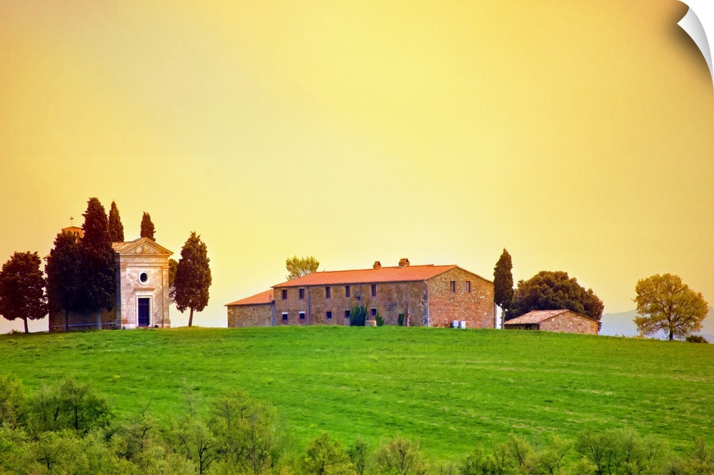 Old traditional Tuscan farm buildings set on a green grass hill with a clear sunset sky.