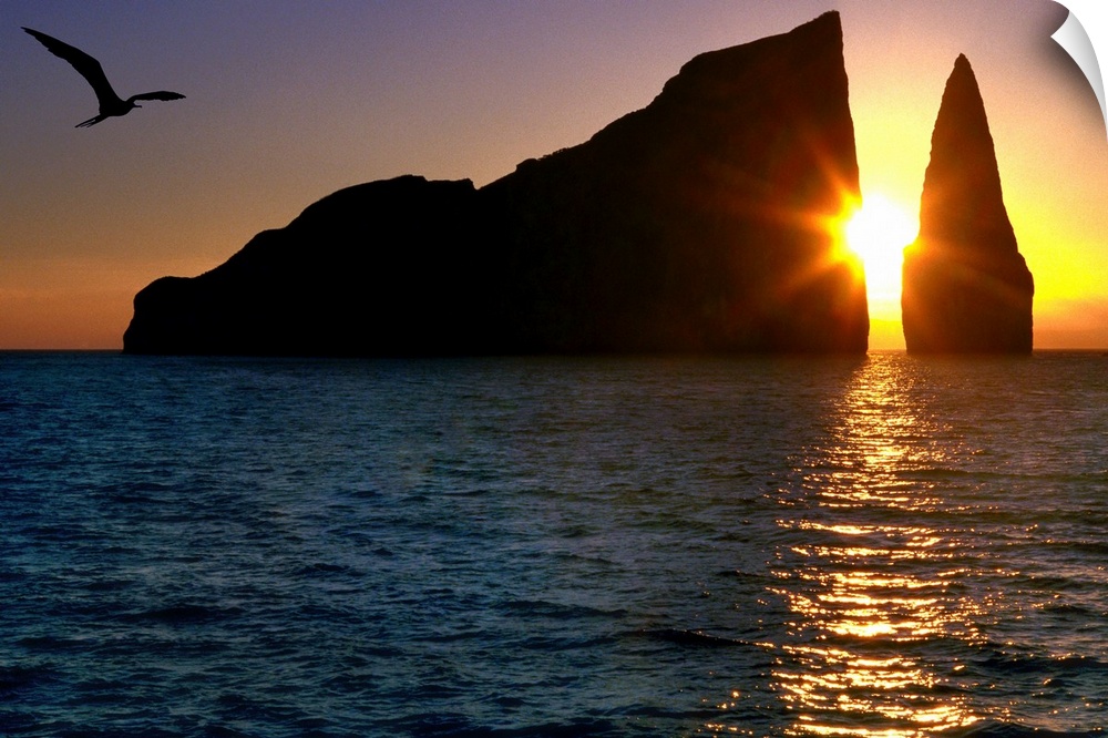 Photograph of the sun setting between two large cliffs over the ocean in the Galapagos.