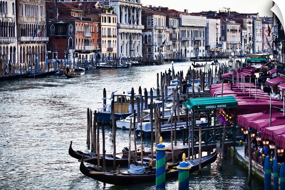 Gondola boats sit in the water which curves toward the back of the picture and is lined on either side by buildings and do...