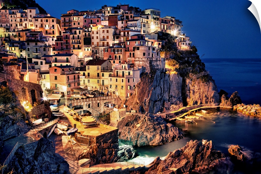 Large photograph taken of homes and buildings sitting within the rocky cliffs of a city in Europe at night.  The bright li...